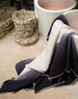 Ink Black White Ombre Textured Throw In Hand Spun Merino And Hand Stitched Hem draped over pottery in a serene setting.