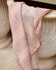 Silica Rose In Shades of Salmon Pink Gray Stripes Pattern Soft Handwoven Merino Throw draped over a decorative pot