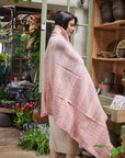 Silica Rose In Shades of Salmon Pink Gray Stripes Pattern Soft Handwoven Merino Throw wrapped around a model in a floral setting.