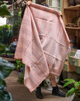 Silica Rose In Shades of Salmon Pink Gray Stripes Pattern Soft Handwoven Merino Throw displayed in a vibrant plant-filled setting.