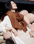 Woman wearing a Coco Brown Hand Woven Linen Silk Blend Scarf against a backdrop of pottery.