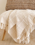 Sea Shell White Textured Checks Handloom Throw displayed on a wooden bench, showcasing its elegant design and hand-rolled fringes.