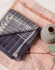 Alloy Dark Blue Stripes Pattern Soft Merino Linen Handloom Throw folded with a decorative vase and greenery.