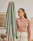Model showcasing the Salvia Green Brown Merino Ombre Handloom Throw in a cozy living room setting.