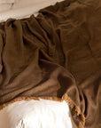 Hay Brown Twill Merino Handwoven Throw draped on a bed, showcasing its soft texture and elegant design.