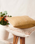 Nira Ochre Hand Spun Organic Cotton Handloom Pillow on a stool beside flowers in a modern vase.
