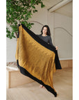 A person holding the Handwoven Topaz Brown Myrtle Drift Merino Throw showcasing its unique pattern and warm colors.