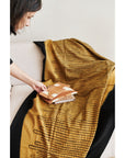 Handwoven Topaz Brown Myrtle Drift Merino Throw draped on a couch with a person holding books.