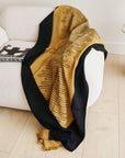 Handwoven Topaz Brown Myrtle Drift Merino Throw draped over a couch, showcasing its unique pattern and color contrast.