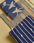 Rosewood Indigo Hand Knotted Stripes Handloom Merino Throw with decorative notebooks on a textured background.