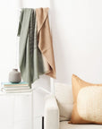 Salvia Green Brown Handwoven Merino Queen Size Bedspread styled on a white ladder with gold shunya silk pillow next to it on a white couch