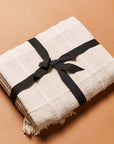 Sea Shell White Textured Checks Handloom Throw wrapped with a black ribbon on a tan background.