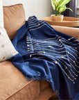 Rosewood Indigo Hand Knotted Stripes Handloom Merino Throw draped on a couch, showcasing its luxurious design and craftsmanship.