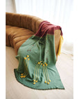 Avocado Green Multi Color Warm Hues Hand Woven Hand Knotted Textured Merino Throw draped on a modern couch.