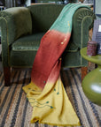 Avocado Green Multi Color Warm Hues Hand Woven Hand Knotted Textured Merino Throw draped over a green chair.