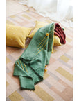 Avocado Green Multi Color Warm Hues Hand Woven Hand Knotted Textured Merino Throw draped over pillows on a soft rug.