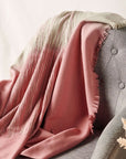 Chive Pink Green Ombre Handloom Merino Throw draped over a gray armchair showcasing its unique colors and textures.