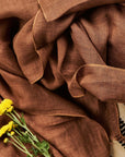 Coco Brown Hand Woven Linen Silk Blend Scarf draped elegantly with yellow flowers.