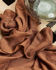 Coco Brown Hand Woven Linen Silk Blend Scarf draped elegantly on a textured surface with a decorative glass bowl.