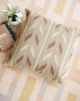 Ero Green Brown Geometric Pattern Hand Woven Large Pillow on a patterned rug with a plant and books.