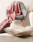 Chive Pink Green Ombre Handloom Merino Throw draped over a gray chair with decorative pillows and a vase.