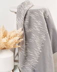 Flo Gray Textured Handloom Merino Throw draped over a chair next to a decorative vase with dried flowers.
