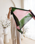 Iris Kiwi Green Pink Cashmere Merino Handwoven Scarf displayed by a model in a bright room with floral decor.