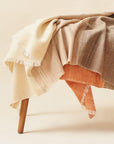 Chestnut Orange Cream Color Block Handwoven Merino Throw draped elegantly over a wooden chair.