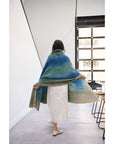 Woman wearing a Lake Moss handwoven merino throw blanket showcasing serene shades of blue green.
