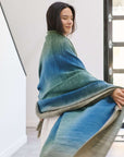 Model draped in Lake Moss handwoven merino throw blanket showcasing serene shades of blue and green.