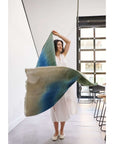 Woman elegantly showcasing the Lake Moss handwoven merino throw blanket in serene shades of blue and green.