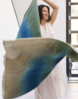 Woman joyfully displaying a Lake Moss Handwoven Merino Throw Blanket in serene shades of blue and green.