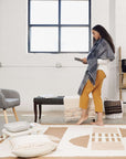 Dyoon Abstract Pattern Handwoven Artisanal Wool Rug displayed in a modern living room setting with a woman admiring it.