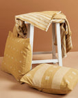 Nira Ochre Hand Spun Organic Cotton Handloom Pillow displayed with a striped throw on a white stool.