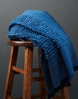 Macaroon Midnight Dark Blue Textured Merino Handloom Throw displayed on a wooden stool.