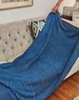 Macaroon Midnight Dark Blue Textured Merino Handloom Throw elegantly draped over a beige sofa.