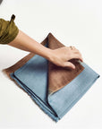 Mahogany Sky Brown Blue Ombre Linen Silk Handloom Scarf being folded by hand to showcase its elegant design.