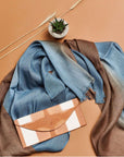 Mahogany Sky Brown Blue Ombre Linen Silk Handloom Scarf draped with a stylish clutch on a beige background.