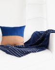 Rosewood Indigo Hand Knotted Stripes Handloom Merino Throw draped on a sofa with a blue and brown decorative pillow.