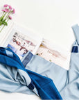 Harbor Blue Silk Merino Hand Woven Hand Embroidered Modern Artisanal Scarf displayed with a photo book and flowers.