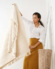A model showcasing the Sea Shell White Textured Checks Handloom Throw, featuring intricately woven checks and hand-rolled fringes.