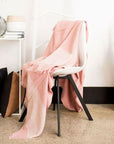 Rosa Plush Maroon Plush Merino Queen Bedspread / Large Throw draped over a chair, showcasing its soft colors and fringes.