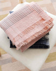 Silica Rose In Shades of Salmon Pink Gray Stripes Pattern Soft Handwoven Merino Throw neatly folded on a chair.