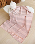 Silica Rose In Shades of Salmon Pink Gray Stripes Pattern Soft Handwoven Merino Throw draped on a modern coffee table.