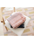 Silica Rose In Shades of Salmon Pink Gray Stripes Pattern Soft Handwoven Merino Throw draped on a chair.