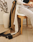 Siro Brown Handwoven Merino Artisan Throw Blanket draped on a chair beside a person holding a color palette.