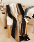 Siro Brown Handwoven Merino Artisan Throw Blanket draped over a chair, showcasing its soft textures and elegant design.