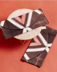 Tisa Artisanal Pouch In Black Pink Triangle Print displayed on a round marble surface against a coral background.