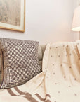Oasis Charcoal Block Print Mulberry Silk Pillow Cover on a sofa with a cozy throw blanket.
