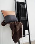 Walnut Black Yak With Hand Knotted Merino Stripes Handloom Throw displayed on a ladder with coordinating cushions.